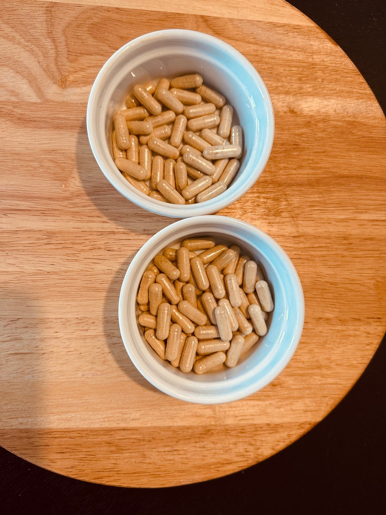 Peut inclure: Deux bols en c&eacute;ramique blanche remplis de capsules beiges. Les bols sont sur une surface en bois.