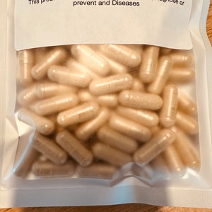Peut inclure: Une image rapproch&eacute;e d'un sac en plastique transparent rempli d'une grande quantit&eacute; de capsules beiges. Le sac est scell&eacute; et porte une &eacute;tiquette blanche avec le texte "Contact for more info (404)784-9433 These product have not be evaluated by the FDA Consult with your physician before use. This product is not intended to, Treat, Cure, Diagnose or prevent and Diseases"