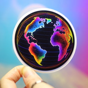May include: A round sticker featuring a colorful, rainbow-hued world map design. The continents are filled with vibrant shades against a black background, with a white border. The sticker is held up by a hand.