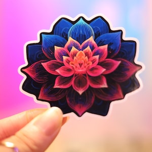 May include: A colorful sticker featuring a detailed lotus flower design. The flower has a gradient of colors, with pink and red petals in the center, transitioning to blue and black on the outer edges. The sticker is held up by a hand.