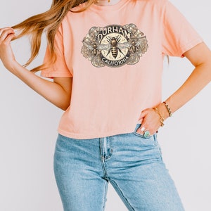 May include: A light pink t-shirt with a graphic of a bee with the text "Durham California" on it.