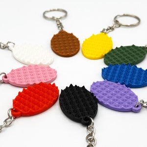 May include: A set of ten colorful keychains with a textured oval shape. The keychains are attached to silver key rings. The colors include pink, red, black, purple, blue, green, yellow, white, and brown.