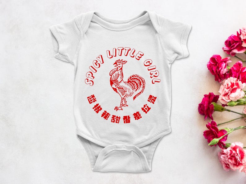 May include: White baby onesie with a red graphic of a rooster and the text "SPICY LITTLE GIRL" in a circular design. The onesie is on a white surface with pink flowers.