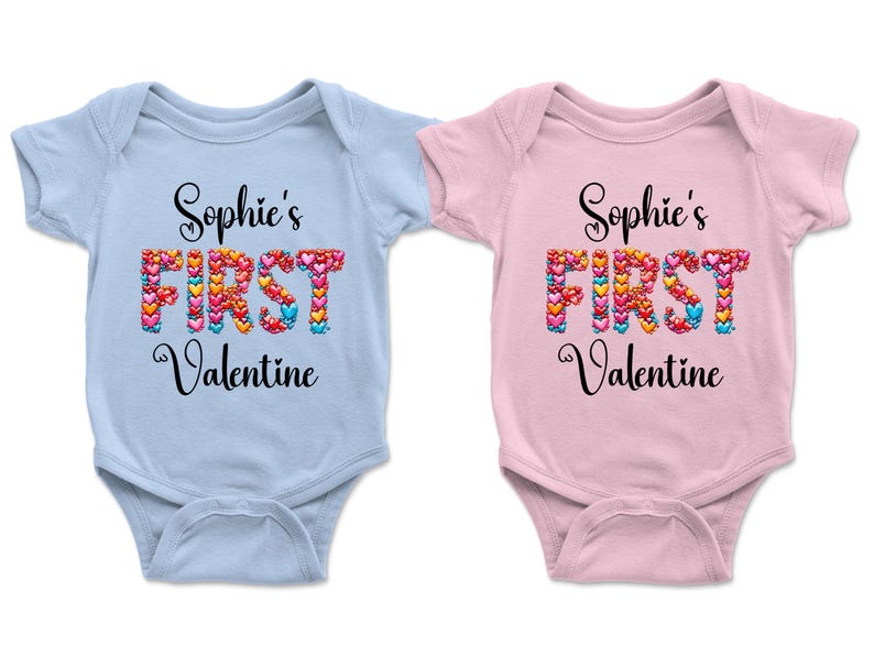 May include: Two baby onesies, one light blue and one pink. Each has the text "Sophie's FIRST Valentine" in black script. The word "FIRST" is made of colorful heart shapes, perfect for a Valentine's Day gift.