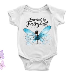 Puede incluir: Body de beb&eacute; blanco con la frase "Powered by Fairydust" en negro. Ilustraci&oacute;n de acuarela de un hada con alas azules. Tres mariposas pastel. Ropa de beb&eacute;, ideal para reci&eacute;n nacidos.