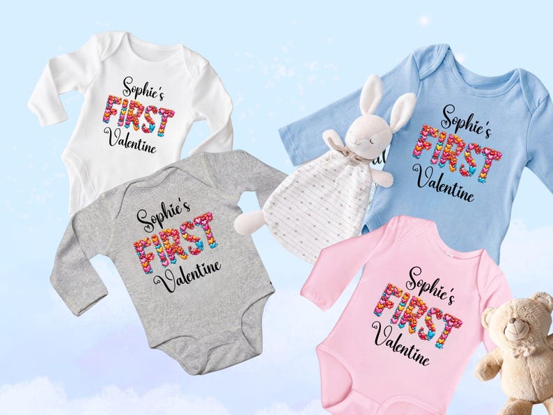 May include: Four baby onesies in white, gray, blue, and pink, each with the text "Sophie's FIRST Valentine." The word "FIRST" is made of colorful hearts. A stuffed bunny and teddy bear are also in the image.