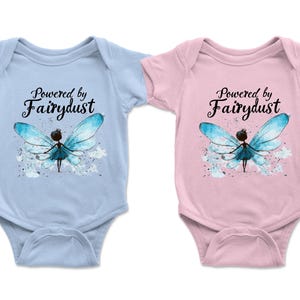 Puede incluir: Dos bodies de beb&eacute;, uno celeste y otro rosa, cada uno con el texto "Powered by Fairydust". Ambos presentan una ilustraci&oacute;n de acuarela de un hada con alas azules. Los bodies est&aacute;n dise&ntilde;ados para beb&eacute;s.