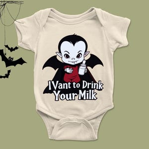 以下が含まれることがあります： ベージュ色のベビーボディスーツ。黒いマントと髪の毛の漫画の吸血鬼がボトルを持ち、「I vant to drink your milk」の文字。ハロウィーンをテーマにしたベビー服。