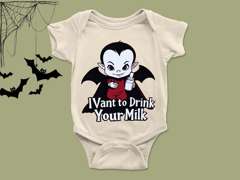 以下が含まれることがあります： ベージュ色のベビーボディスーツ。黒いマントと髪の毛の漫画の吸血鬼がボトルを持ち、「I vant to drink your milk」の文字。ハロウィーンをテーマにしたベビー服。