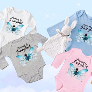 Puede incluir: Cuatro bodies de beb&eacute; en blanco, gris, azul y rosa, cada uno con un dise&ntilde;o de manga larga. El texto "Powered by Fairydust" est&aacute; impreso sobre una ilustraci&oacute;n de hada con alas azules. Un conejito de peluche y un osito de peluche tambi&eacute;n est&aacute;n en la imagen.