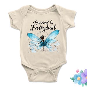 Puede incluir: Body de beb&eacute; color crema con el texto "Powered by Fairydust" en escritura negra. Ilustraci&oacute;n de acuarela de un hada con alas azules y salpicaduras de acuarela azules.