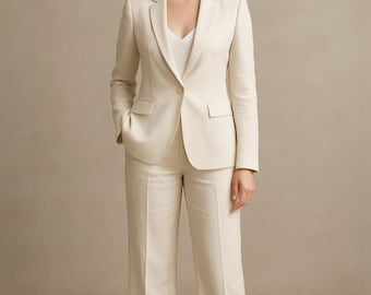 May include: A cream-colored suit consisting of a blazer and matching pants. The blazer has a single-button closure and two front pockets. The pants are wide-legged. The outfit is worn with a white top. A black square with a white logo is in the background.