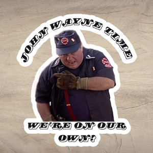 May include: A sticker featuring a photo of John Wayne from the movie "We're No Angels" with the text "John Wayne Time" above his head and "We're On Our Own?" below.