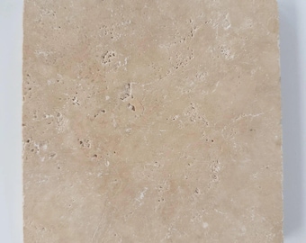 May include: A square travertine tile featuring a natural beige color palette with a porous, pitted surface texture. The stone displays organic variations in tone and small, irregular indentations across its flat, matte finish.
