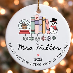 Puede incluir: Adorno navide&ntilde;o redondo de cer&aacute;mica blanca con una cuerda dorada. El adorno presenta un dise&ntilde;o de bola de nieve, libros y un mu&ntilde;eco de nieve. El texto dice "Mrs. Miller" y "Thank you for being part of my story" con el a&ntilde;o 2025.