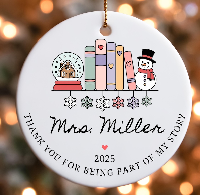 Puede incluir: Adorno navide&ntilde;o redondo de cer&aacute;mica blanca con una cuerda dorada. El adorno presenta un dise&ntilde;o de bola de nieve, libros y un mu&ntilde;eco de nieve. El texto dice "Mrs. Miller" y "Thank you for being part of my story" con el a&ntilde;o 2025.