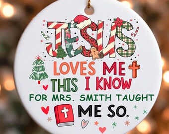 May include: A white ceramic Christmas ornament with the words "JESUS LOVES ME THIS I KNOW FOR MRS. SMITH TAUGHT ME SO." The word "JESUS" is decorated with Christmas patterns. The ornament has a gold string for hanging.