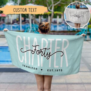 May include: A turquoise beach towel with the text "Chapter Forty" in white lettering and "Jennifer Est. 1975" in black lettering.
