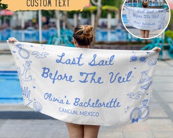 May include: White beach towel with blue text and illustrations. The towel reads "Last Sail Before The Veil, Olivia's Bachelorette, Cancun, Mexico." Decorative elements include rings, seashells, and sunglasses.