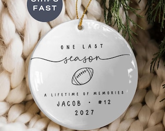 Puede incluir: Un adorno de cerámica blanca redonda con texto negro que dice ONE LAST season A LIFETIME OF MEMORIES JACOB #12 2027 y un dibujo lineal de un balón de fútbol americano en el centro. El adorno cuelga de un cordón dorado sobre un fondo blanco.
