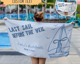 May include: A light gray beach towel with the text "LAST SAIL BEFORE THE VEIL" in dark blue. A sailboat graphic and the text "Sophia's Bachelorette, Miami, Florida" are also featured. The towel is held up by a person.