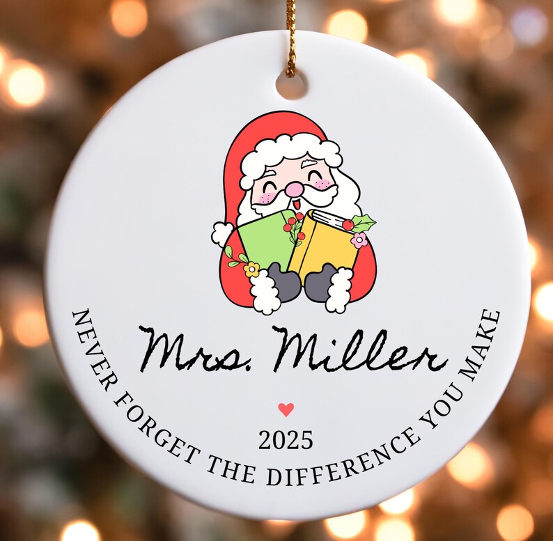 Puede incluir: Adorno navide&ntilde;o redondo de cer&aacute;mica blanca con una ilustraci&oacute;n de Pap&aacute; Noel sosteniendo libros. El adorno incluye el texto "Mrs. Miller", un coraz&oacute;n, el a&ntilde;o "2025" y la frase "Never forget the difference you make".