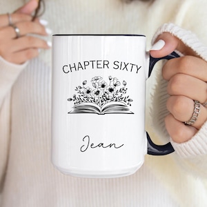 May include: White ceramic mug with a black rim and handle. The mug features the text "CHAPTER SIXTY" above a floral illustration and the name "Jean" in cursive. The design is black and white.
