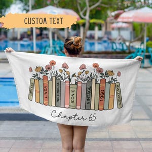 May include: A white beach towel with a row of colorful books with floral accents. The text "Chapter 65" is printed below the books. The words "Timeless", "Linda", "Historical", "Iconic", "Vintage", "1960", and "Masterpiece" are printed on the spines of the books.