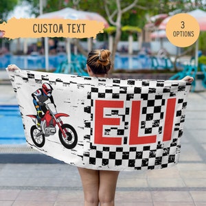 May include: A white beach towel with a black and white checkered pattern. A red and white dirt bike with a rider is on the left side of the towel. The name "ELI" is written in red letters on the right side of the towel.