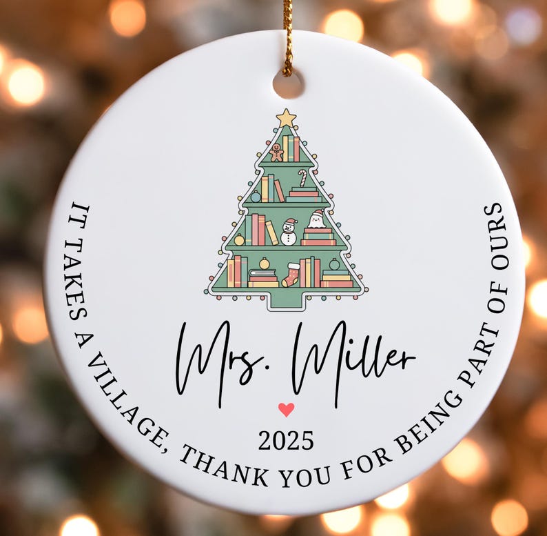 Puede incluir: Adorno navide&ntilde;o redondo de cer&aacute;mica blanca con una cuerda dorada. El adorno presenta un dise&ntilde;o de &aacute;rbol de Navidad hecho de libros, un mu&ntilde;eco de nieve y una estrella. El texto incluye "Mrs. Miller", "2025" y "It takes a village, thank you for being part of ours."