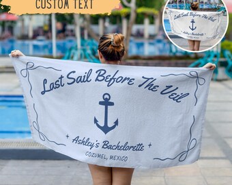 May include: A light gray beach towel with the text "Last Sail Before The Veil" and an anchor graphic. The towel also includes "Ashley's Bachelorette" and "COZUMEL, MEXICO". The towel is held up in front of a pool.
