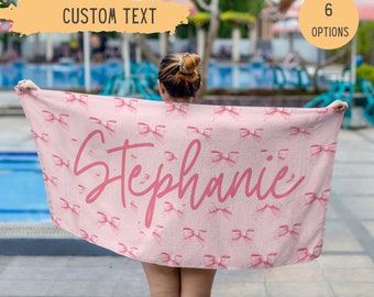May include: Pink beach towel with a white background and a pink bow pattern. The towel has the name "Stephanie" written in pink cursive.