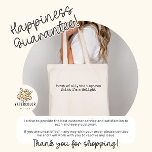 May include: Cream-colored tote bag with the text "first of all, the umpires think I'm a delight." The bag has long handles and is held by a person. The words "Happiness Guarantee!" are written above the bag.