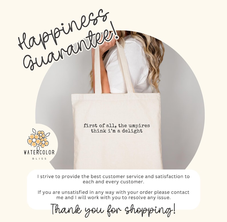 May include: Cream-colored tote bag with the text "first of all, the umpires think I'm a delight." The bag has long handles and is held by a person. The words "Happiness Guarantee!" are written above the bag.