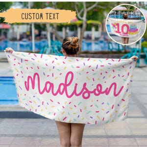 May include: A white beach towel with a pink script name "Madison" and colorful confetti sprinkles. The towel also has the text "Custom Text" in a yellow banner. A smaller image shows a similar towel with "10" and a cake.
