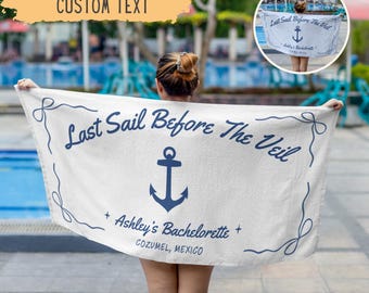 May include: White beach towel with the text "Last Sail Before The Veil" in navy blue, along with an anchor graphic. The towel also includes "Ashley's Bachelorette" and "COZUMEL, MEXICO". The towel is held up by a person.