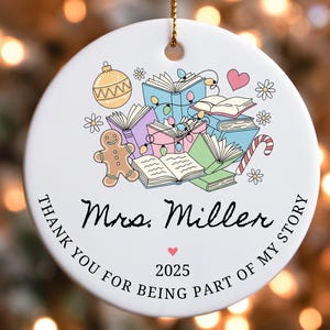 Puede incluir: Un adorno navide&ntilde;o de cer&aacute;mica blanca con una cuerda dorada. El adorno presenta una colorida ilustraci&oacute;n de libros, un hombre de jengibre y un bast&oacute;n de caramelo. El texto dice "Mrs. Miller" y "Thank you for being part of my story 2025."