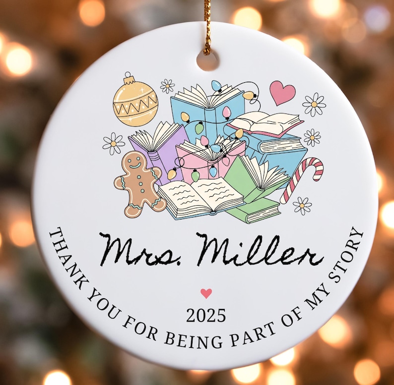 Puede incluir: Un adorno navide&ntilde;o de cer&aacute;mica blanca con una cuerda dorada. El adorno presenta una colorida ilustraci&oacute;n de libros, un hombre de jengibre y un bast&oacute;n de caramelo. El texto dice "Mrs. Miller" y "Thank you for being part of my story 2025."