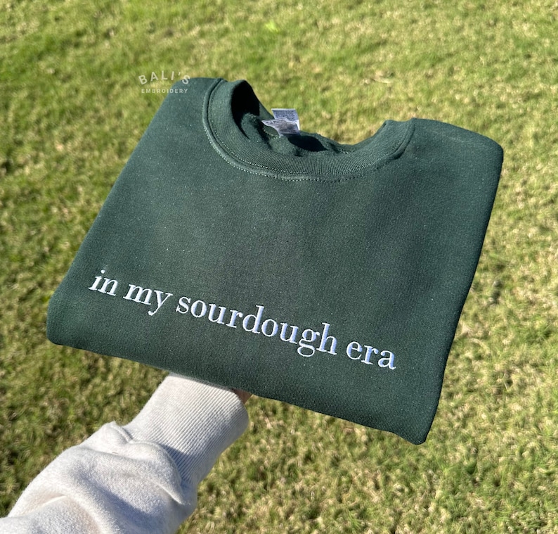 May include: A dark green sweatshirt with the text "in my sourdough era" embroidered in white on the front.
