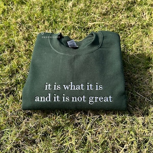 May include: A dark green sweatshirt with the text "it is what it is and it is not great" embroidered in white.