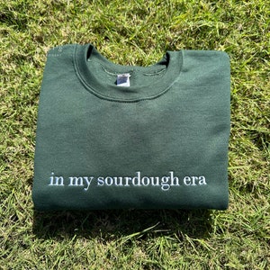 May include: A dark green sweatshirt with the text "in my sourdough era" embroidered in white on the front.