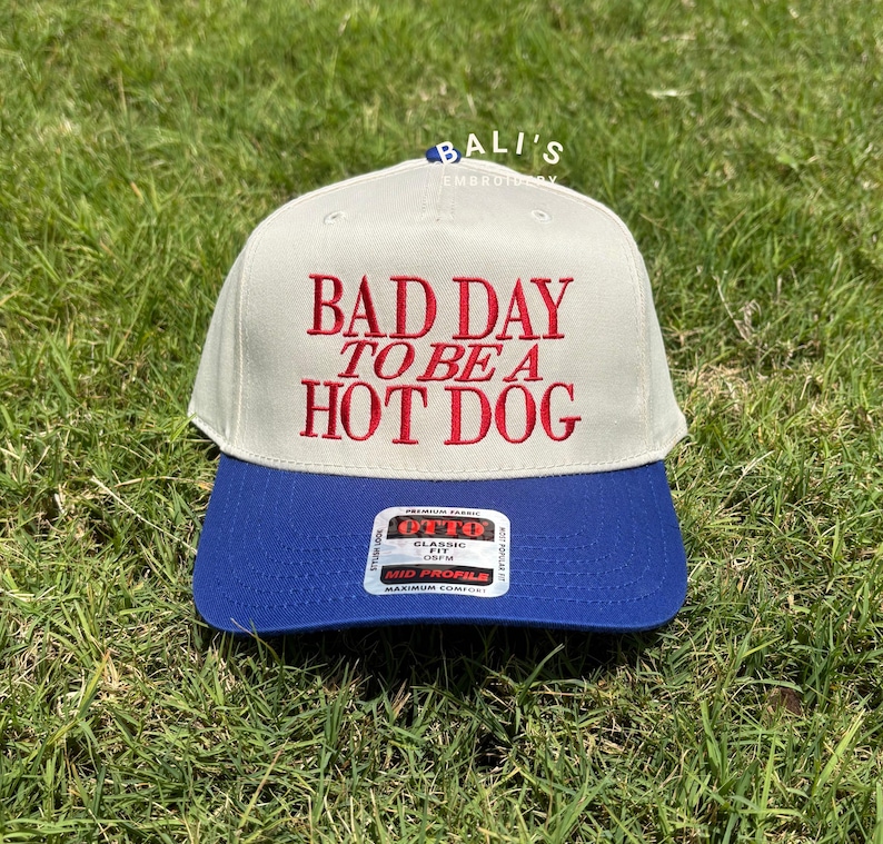 May include: A beige and blue baseball cap with the text "BAD DAY TO BE A HOT DOG" embroidered in red on the front.