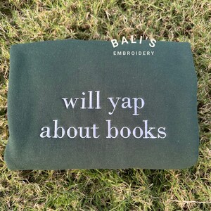 May include: A dark green sweatshirt with white embroidery that says "Bali's Embroidery" and "will yap about books".