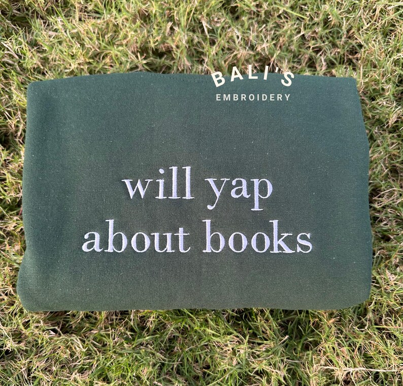 May include: A dark green sweatshirt with white embroidery that says "Bali's Embroidery" and "will yap about books".