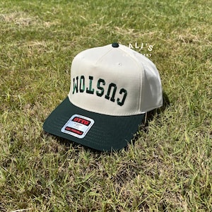 Puede incluir: Una gorra de b&eacute;isbol blanca y verde con la palabra "CUSTOM" bordada en verde en la parte delantera. La gorra tiene una visera verde y una etiqueta blanca con el texto "OTTO CLASSIC FIT" en el lateral.