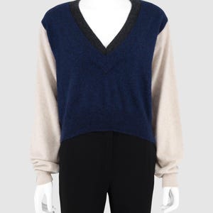 May include: A long-sleeve sweater featuring a deep V-neckline with a dark gray trim. The main body of the sweater is a textured navy blue, while the sleeves are a contrasting light beige color. The garment is displayed on a white mannequin.