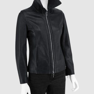 Peut inclure: Veste en cuir noire avec un col montant et une fermeture éclair argentée. La veste a des manches longues et une coupe ajustée, avec un design élégant et moderne. La veste est présentée sur un mannequin.