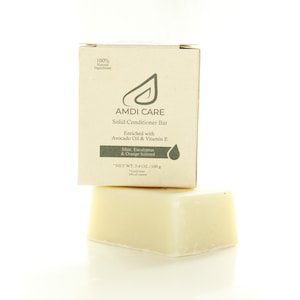 Op de afbeelding: Een bruine kartonnen doos met een wit label waarop staat "AMDI CARE Solid Conditioner Bar Enriched with Avocado Oil & Vitamin E Mint, Eucalyptus & Orange Scented NET WT: 3.4 OZ/100g". De doos ligt op een witte vaste conditioner bar.