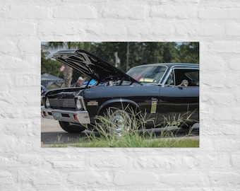 May include: A black Chevrolet Camaro with the hood open, revealing the engine. The car is parked on a grassy area with other cars in the background. The car has a "350" badge on the side.