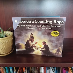 May include: A hardcover book titled "Knots on a Counting Rope" by Bill Martin Jr. and John Archambault, illustrated by Ted Rand. The cover art depicts two figures by a fire, with a "Reading Rainbow Book" sticker.